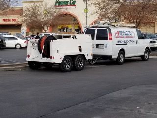 White plumbing van and trailer parked in front of a grocery store.