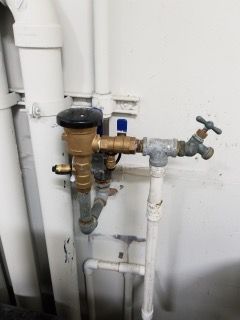 Water valve and pipes connected to a spigot on a white wall. Brass and gray metal components.