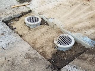 Two circular grates installed in a concrete surface, surrounded by dirt and construction.