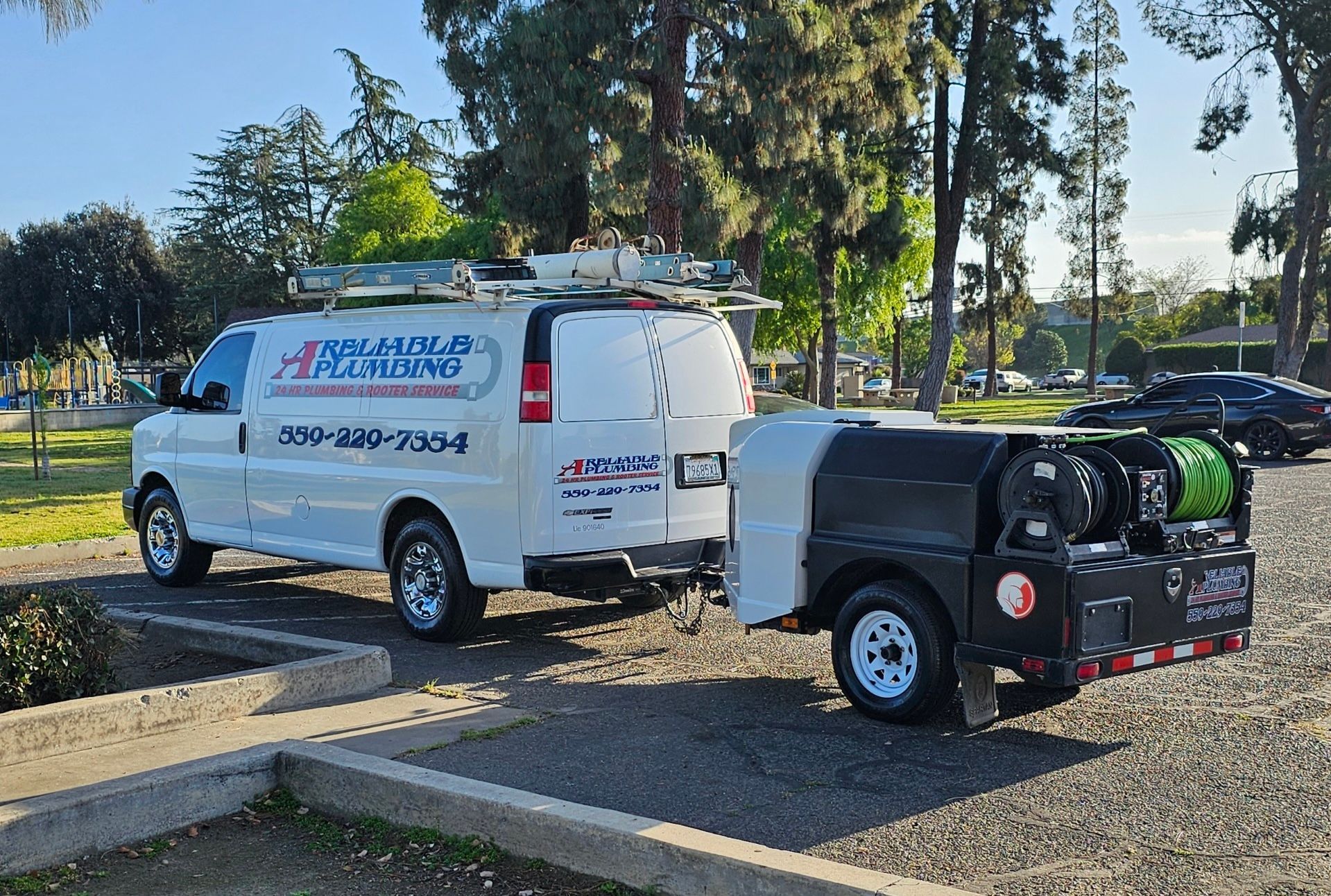 White plumbing van with trailer, parked in a lot.  Van has company logo and phone number.