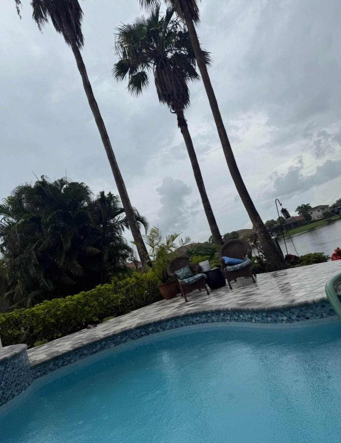 Poolside resort with blue water, palm trees, and lounge chairs under a cloudy sky