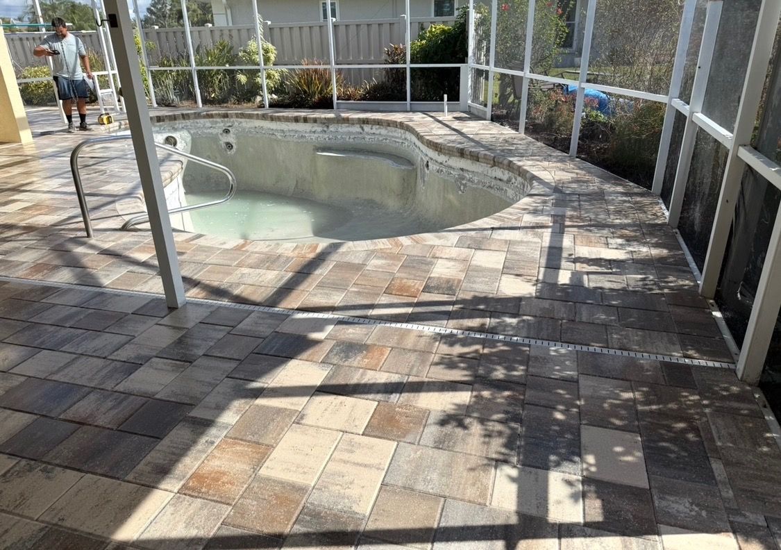 Patio area with a small pool, brick pavers, and a chain-link fence in bright sunlight