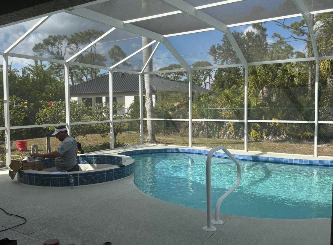 Screened-in backyard pool with a person sitting in a spa beside blue water and palm trees