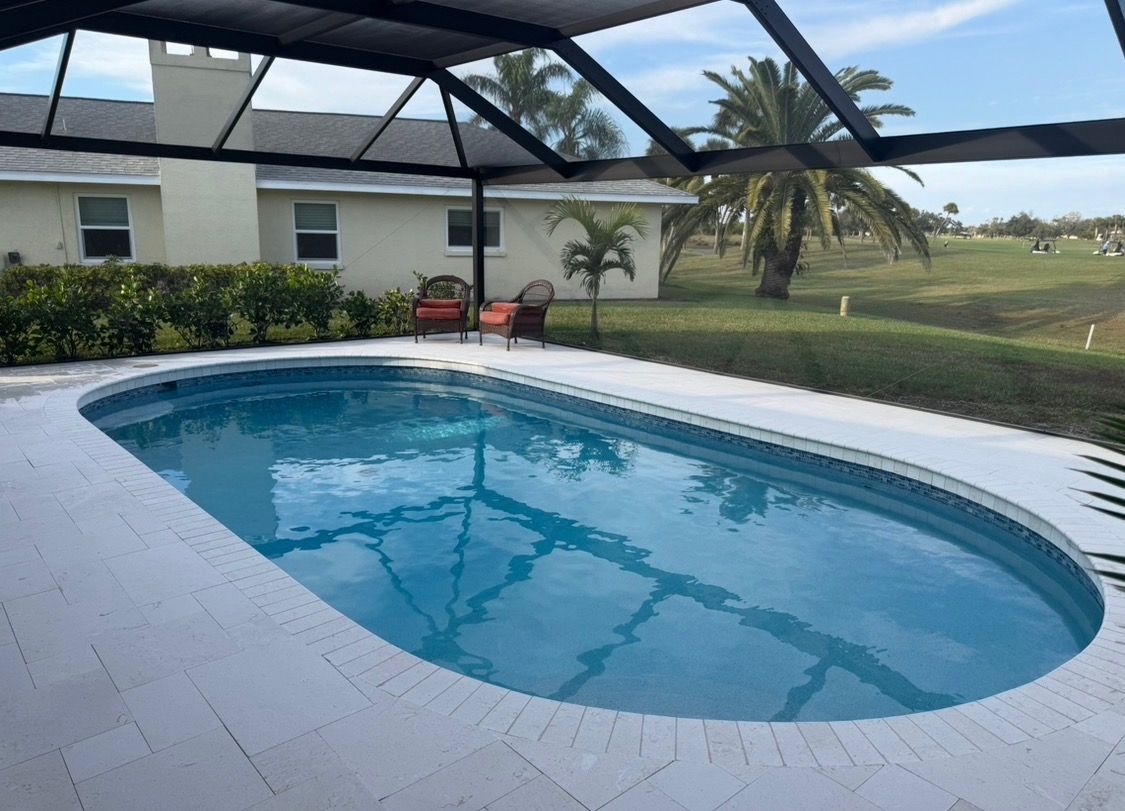 Covered backyard pool beside a white house, with blue water and a grassy view beyond