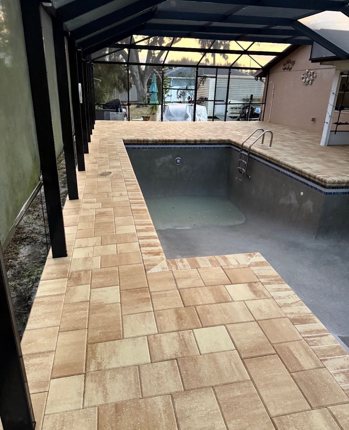 Covered backyard pool with tan stone pavers and black roof beams