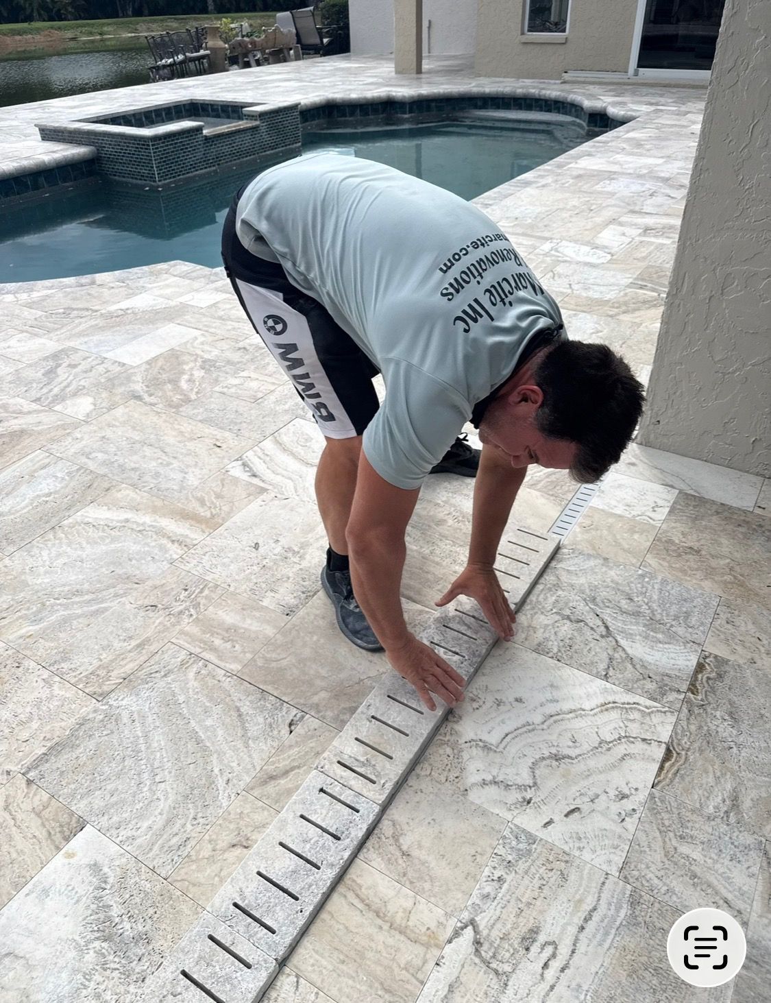 Worker measuring stone pool deck with a tape measure beside a swimming pool
