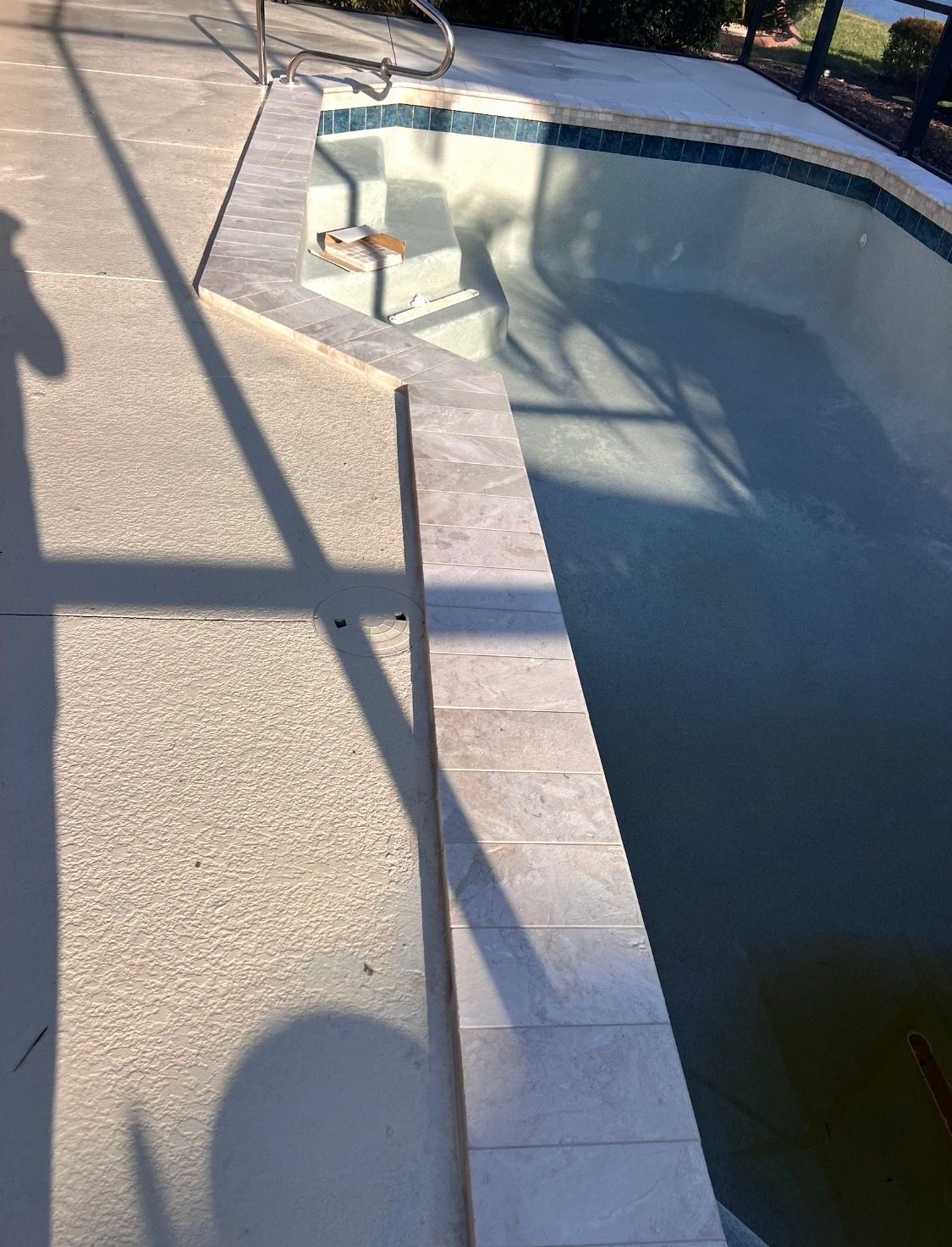 Empty outdoor swimming pool with blue-tiled edge and tan deck in sunlight