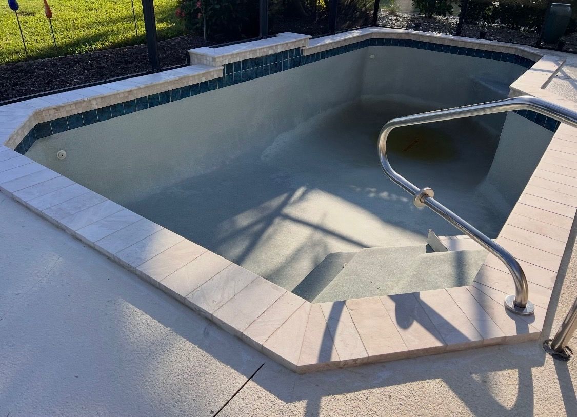 Empty in-ground swimming pool with light blue interior and metal handrail on the deck