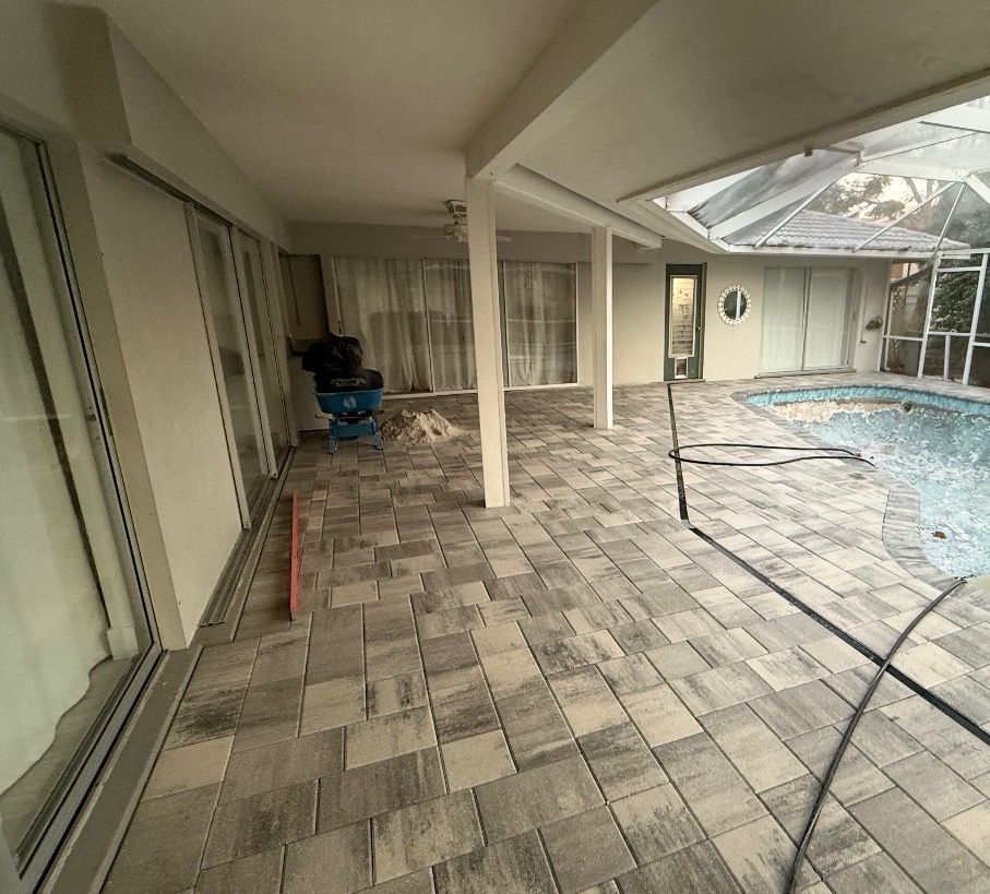 Covered patio with gray pavers beside a swimming pool and sliding glass doors