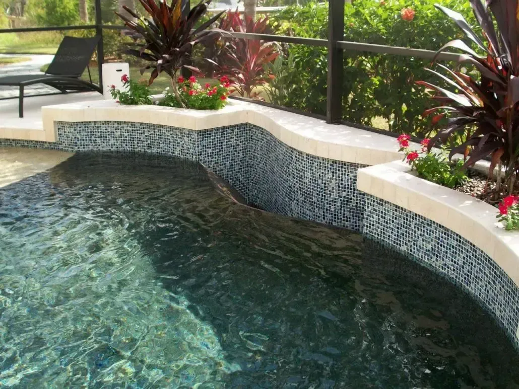 Pool with dark blue mosaic tile and a waterfall feature, surrounded by landscaping.