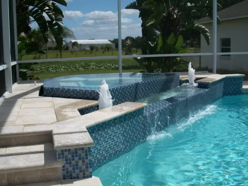 Pool with cascading water feature, spa, and fountains, surrounded by blue tile and beige stone.