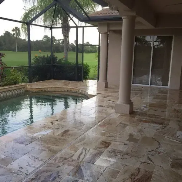 Patio with a pool and wet stone floor, enclosed by a screen, looking out onto a lawn.