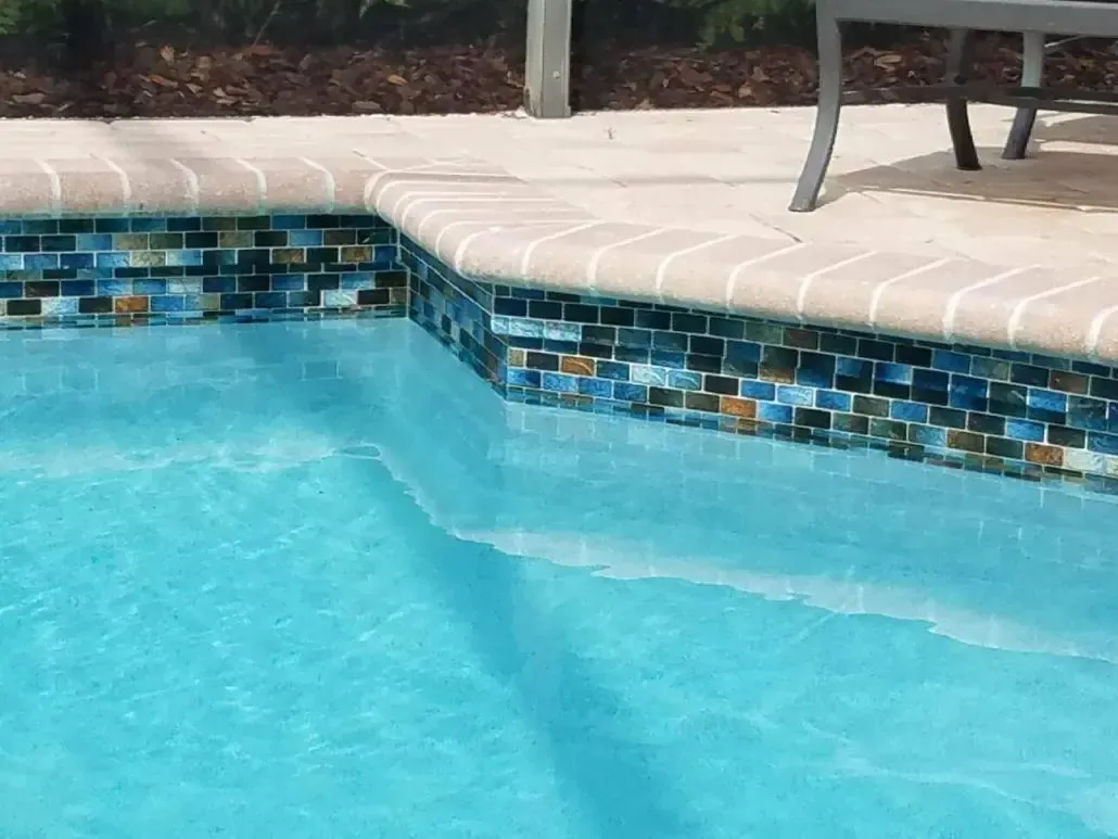 Swimming pool with blue water and mosaic tile trim, brick coping.