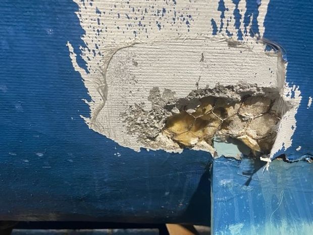 Damaged blue surface with a large area of missing material, revealing underlying layers of filler and insulation.