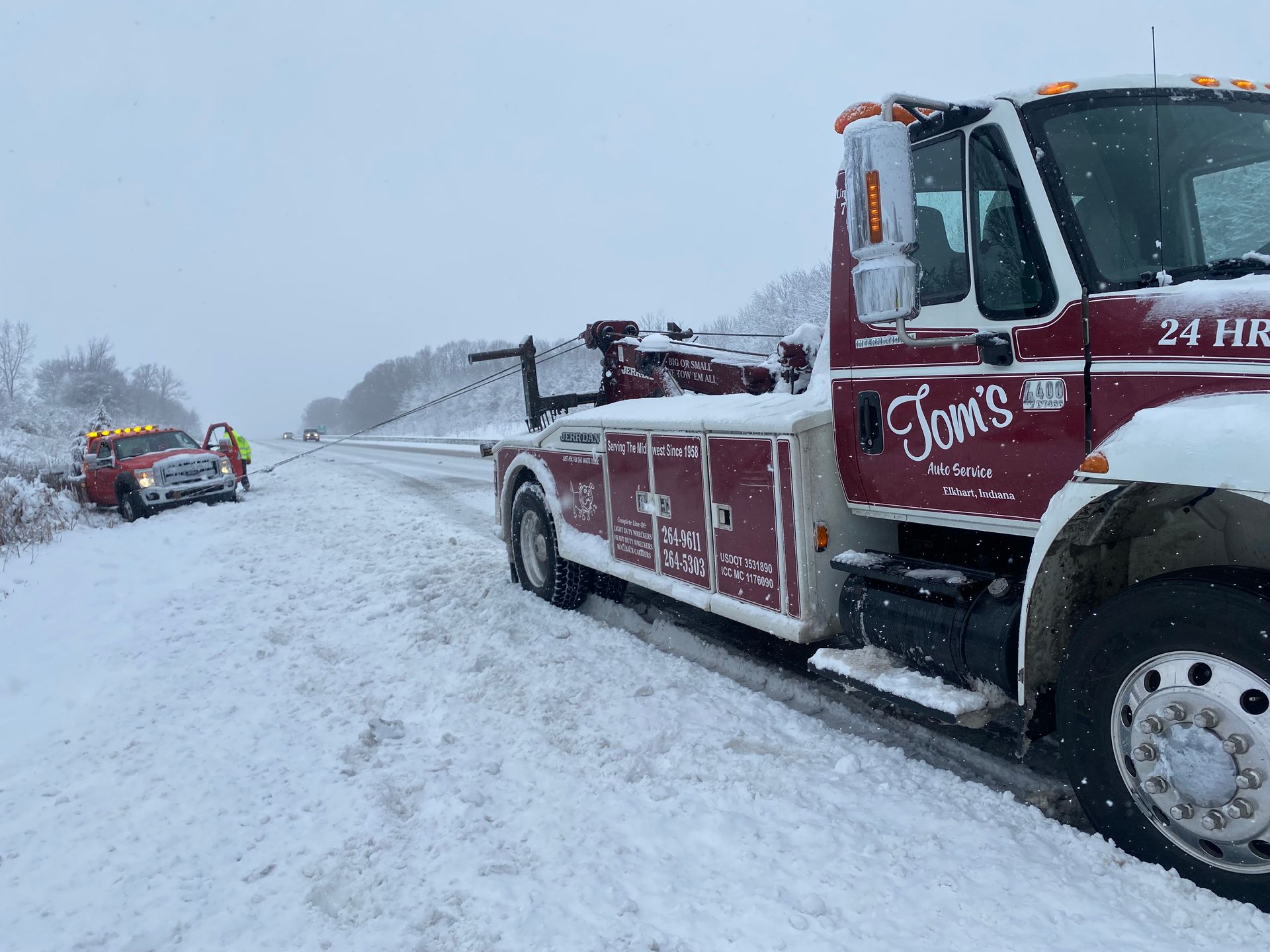 Tow truck assisting a vehicle stuck on a snowy highway. Red tow truck and car with snow-covered ground.