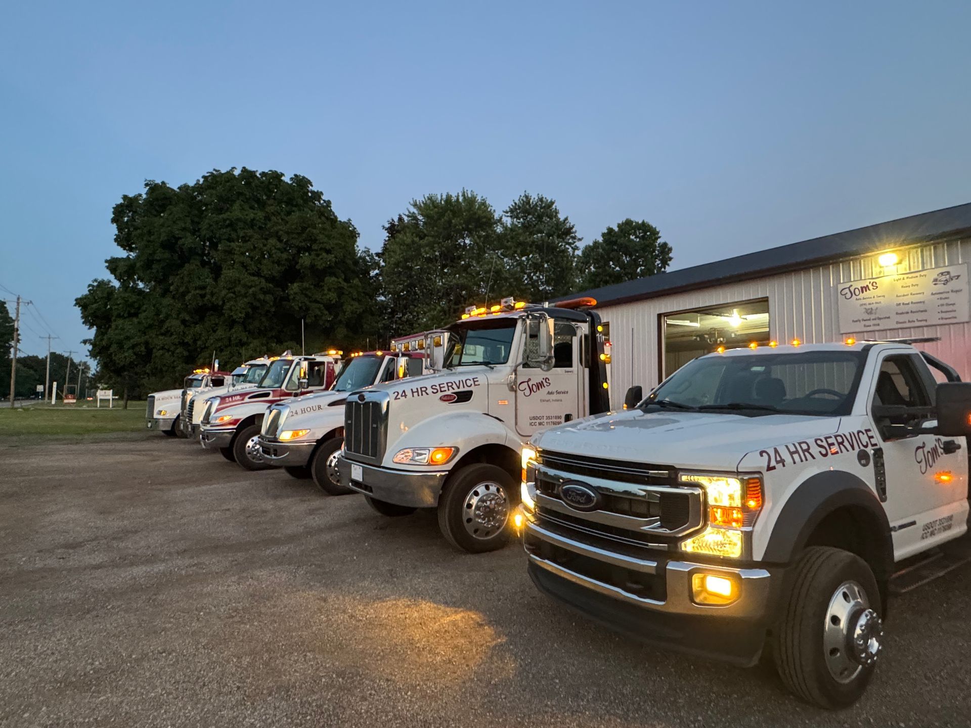 A row of white tow trucks parked outside a building at dusk. 