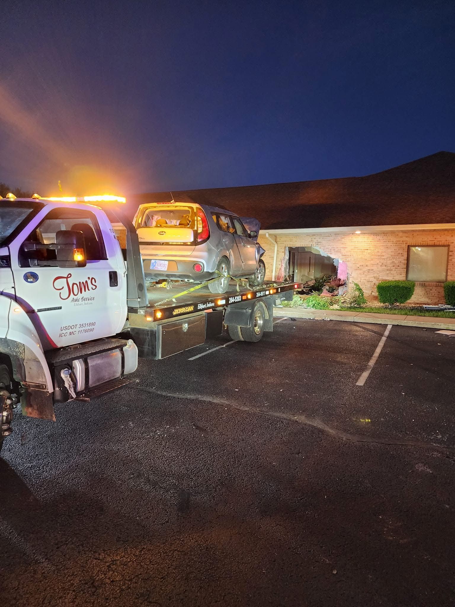 Tow truck loading a car that crashed into a building at night.