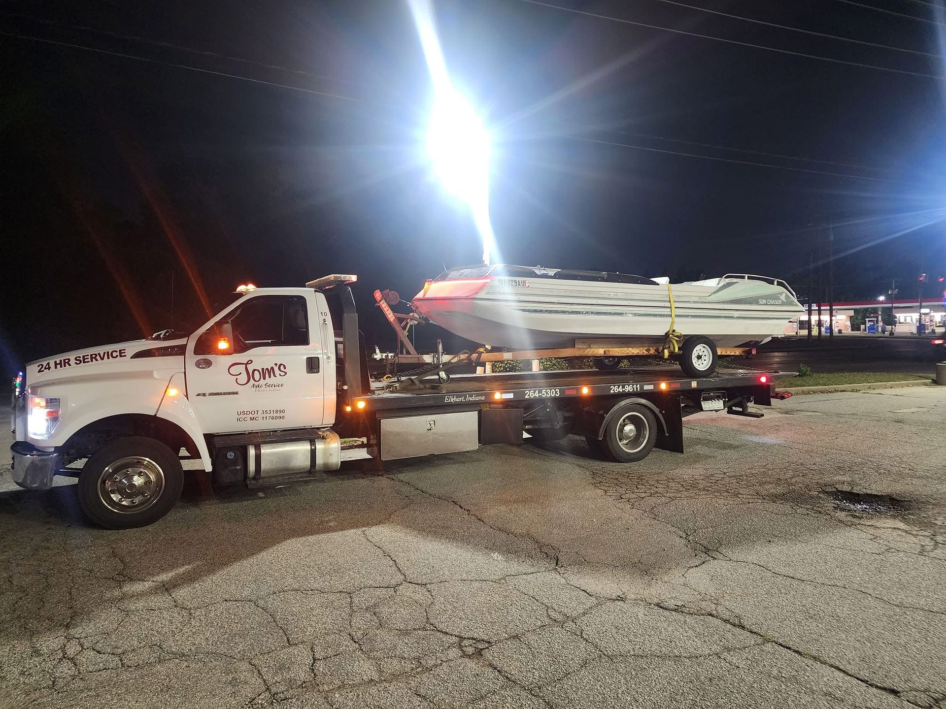 Tow truck with a boat on its flatbed at night.