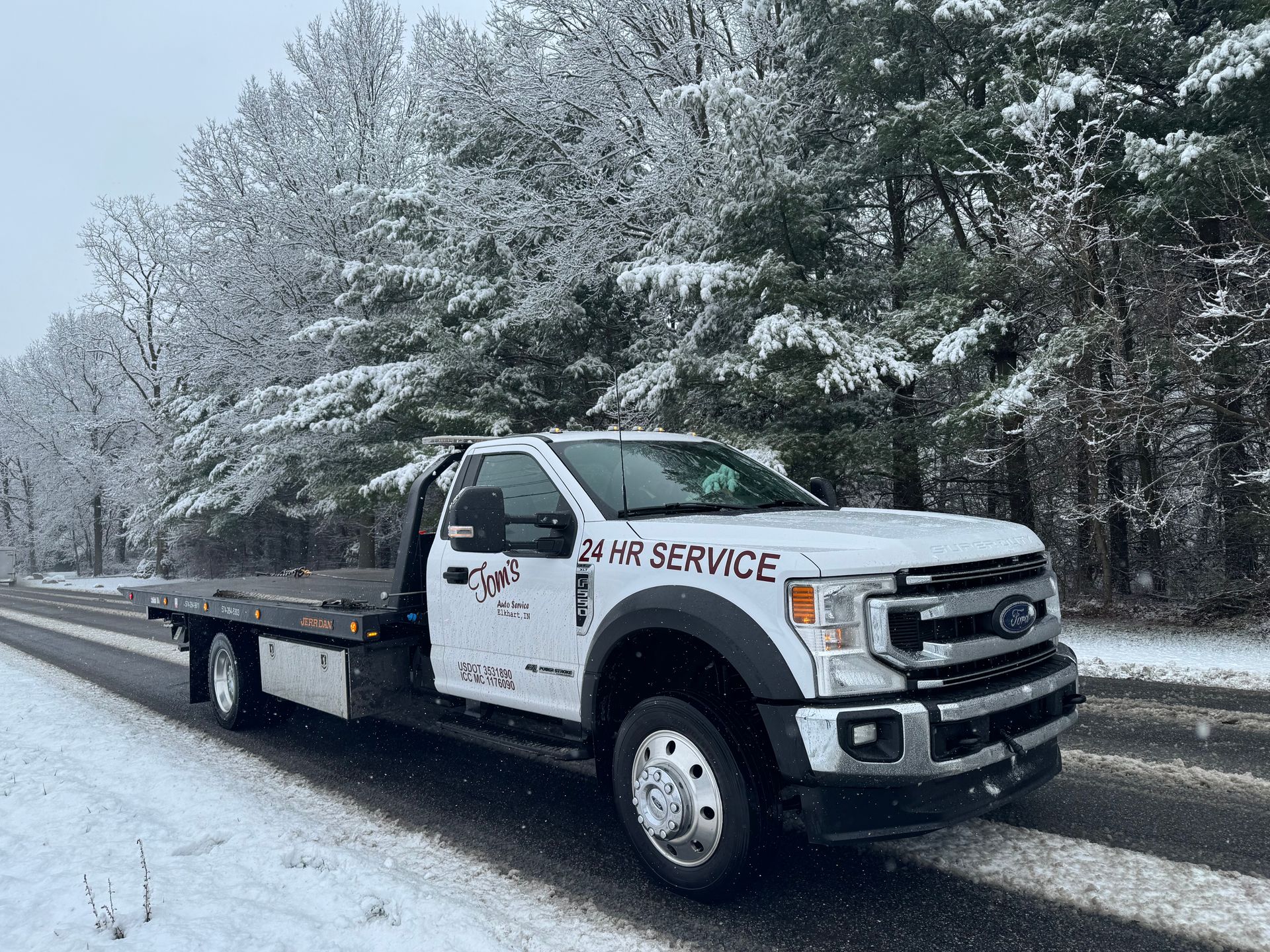 Flatbed tow truck on snowy road, text on truck says 
