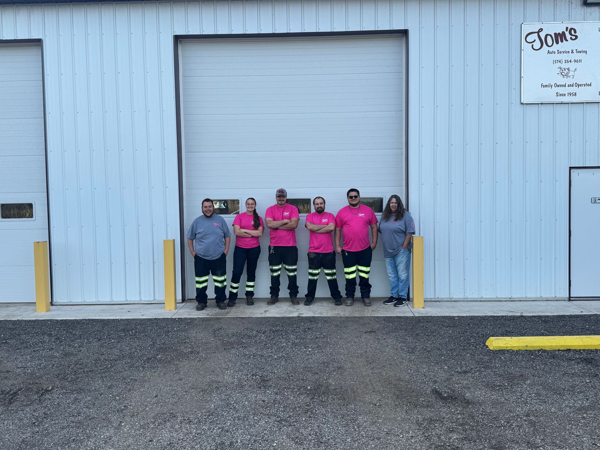 Group of seven people in work attire stand in front of a white building with a garage door.