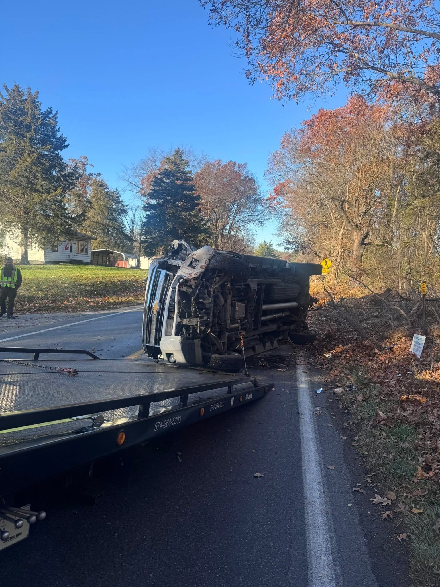Rolled over truck on roadside being towed; fall foliage and sunny day.