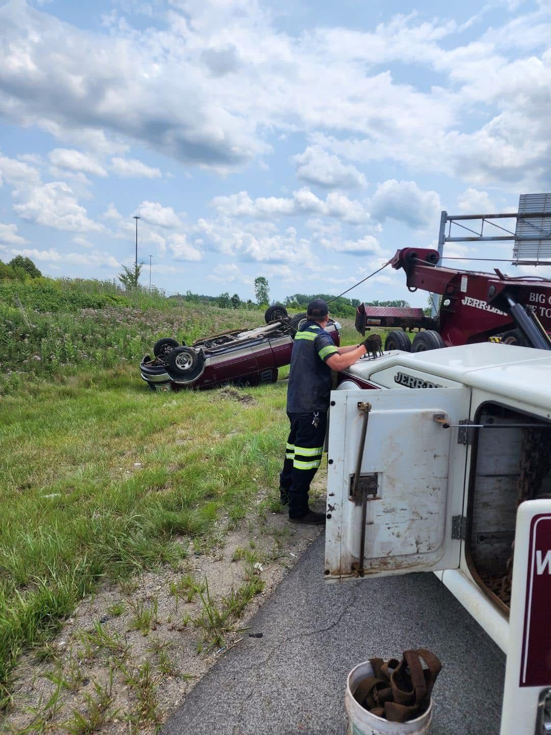 Tow truck operator preparing to upright a flipped car on roadside.
