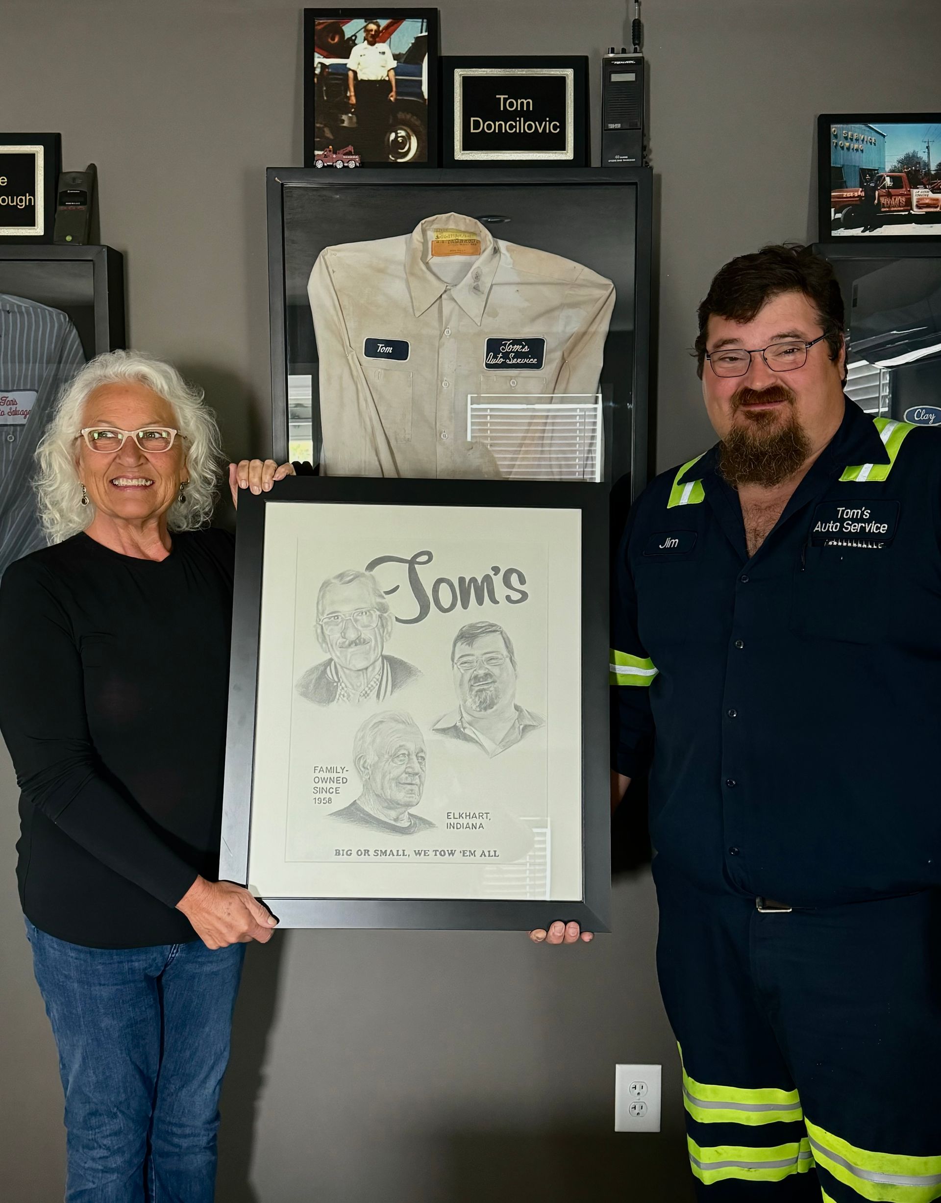 Woman and man holding a framed pencil sketch, with a shirt in a shadow box behind them.