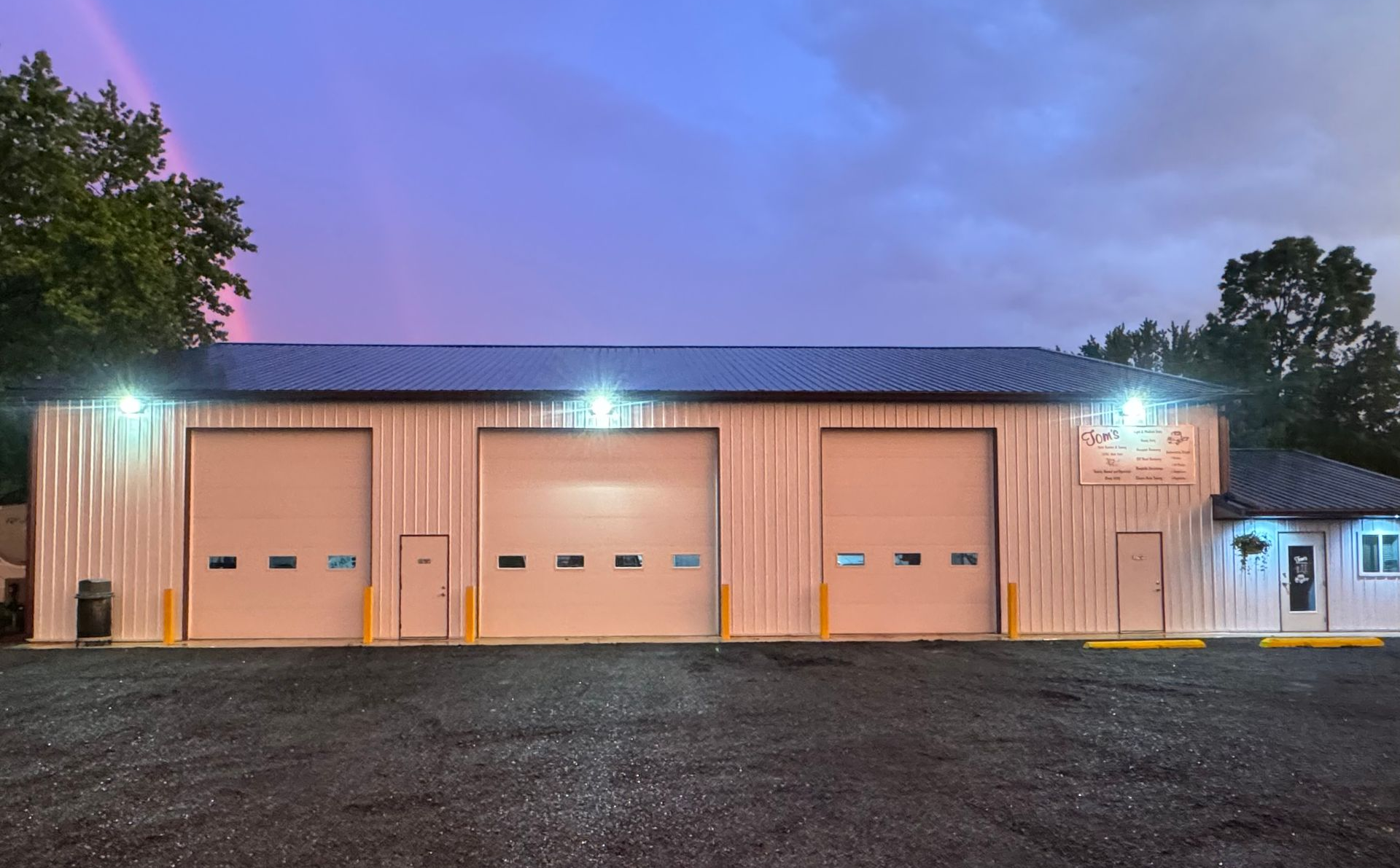 Garage with three bay doors, metal siding, and a small office under a rainbow.