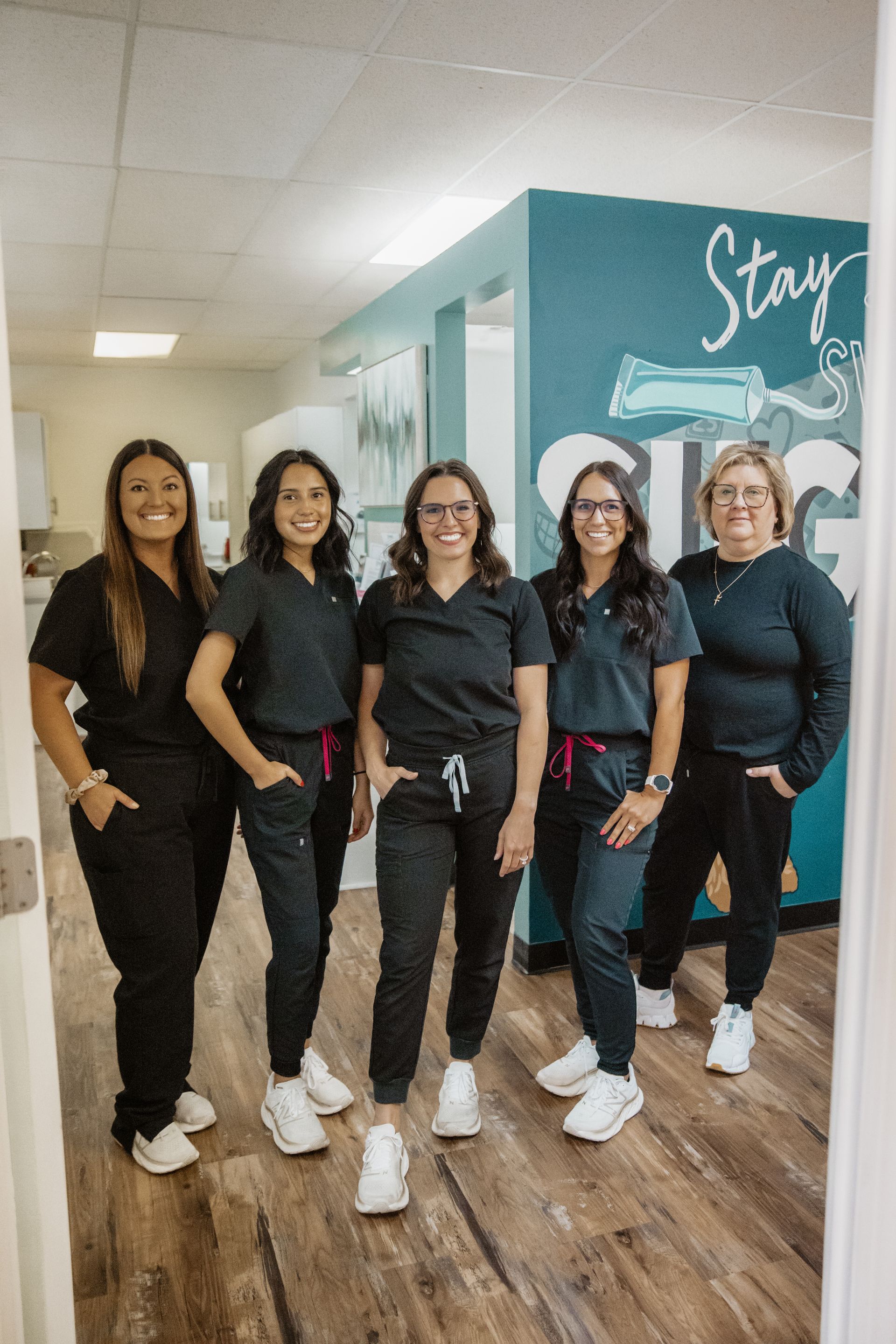 A group of women in scrubs are posing for a picture in a dental office.