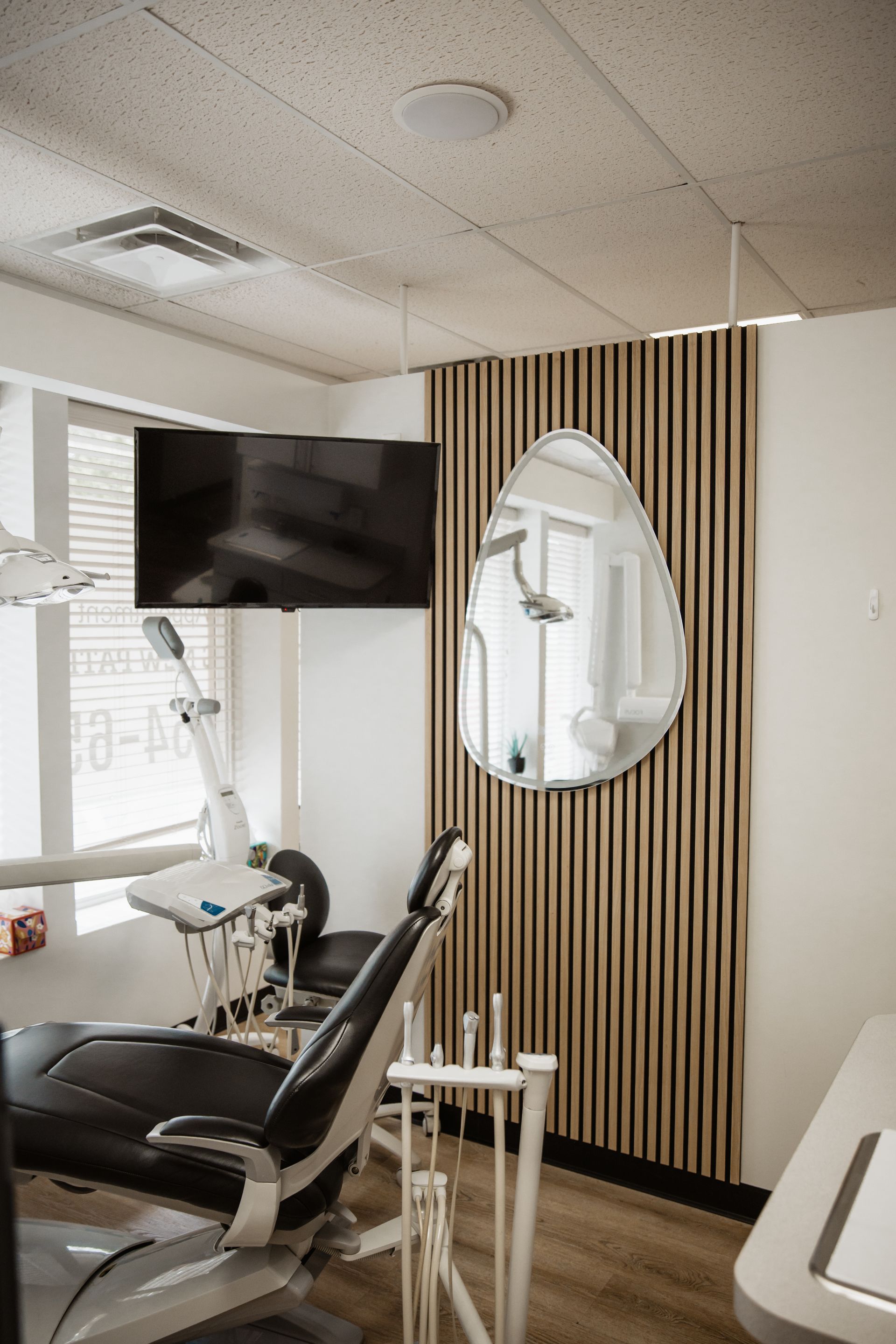 A dental office with a dental chair , television , and mirror.