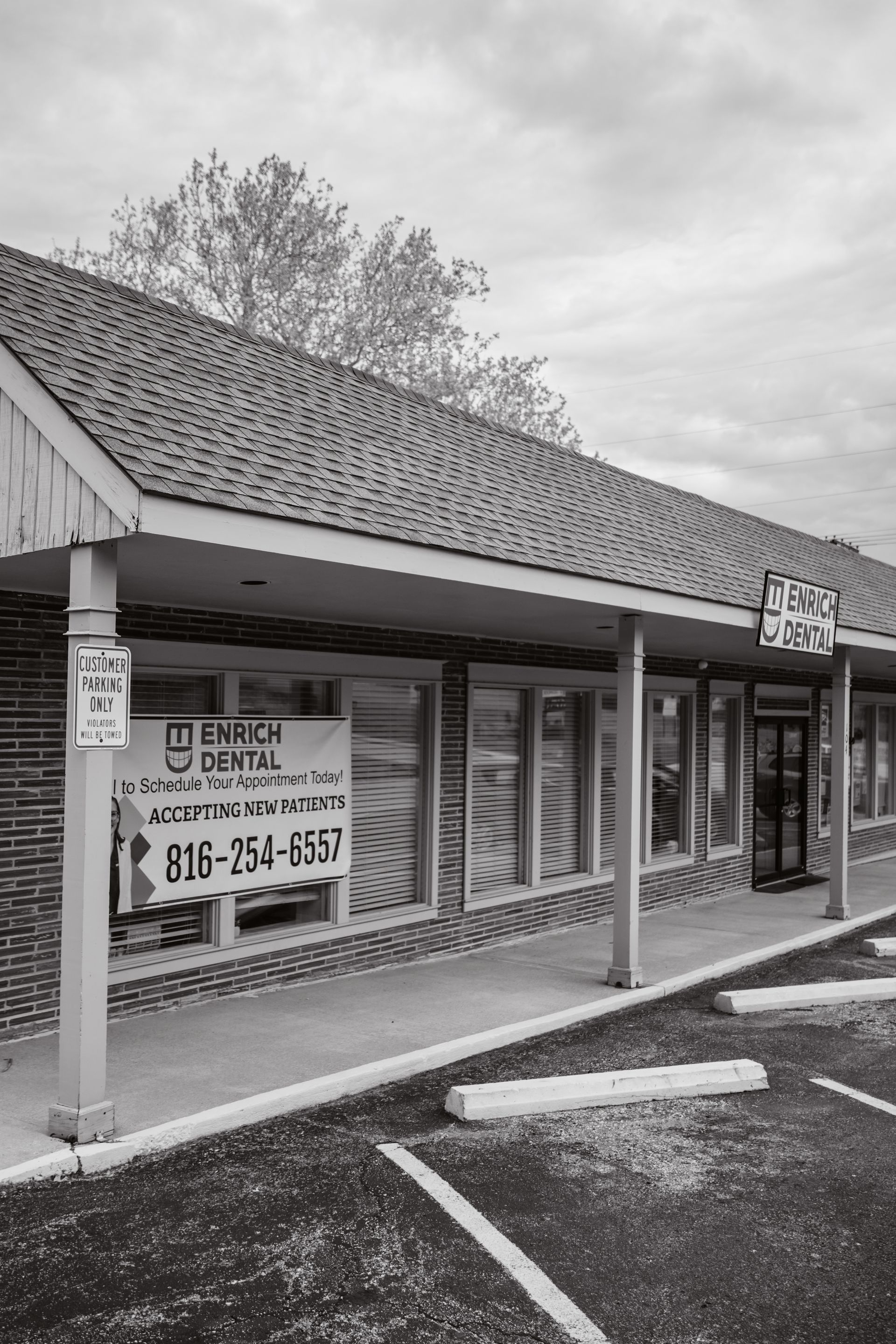 A black and white photo of a brick building with a parking lot in front of it.