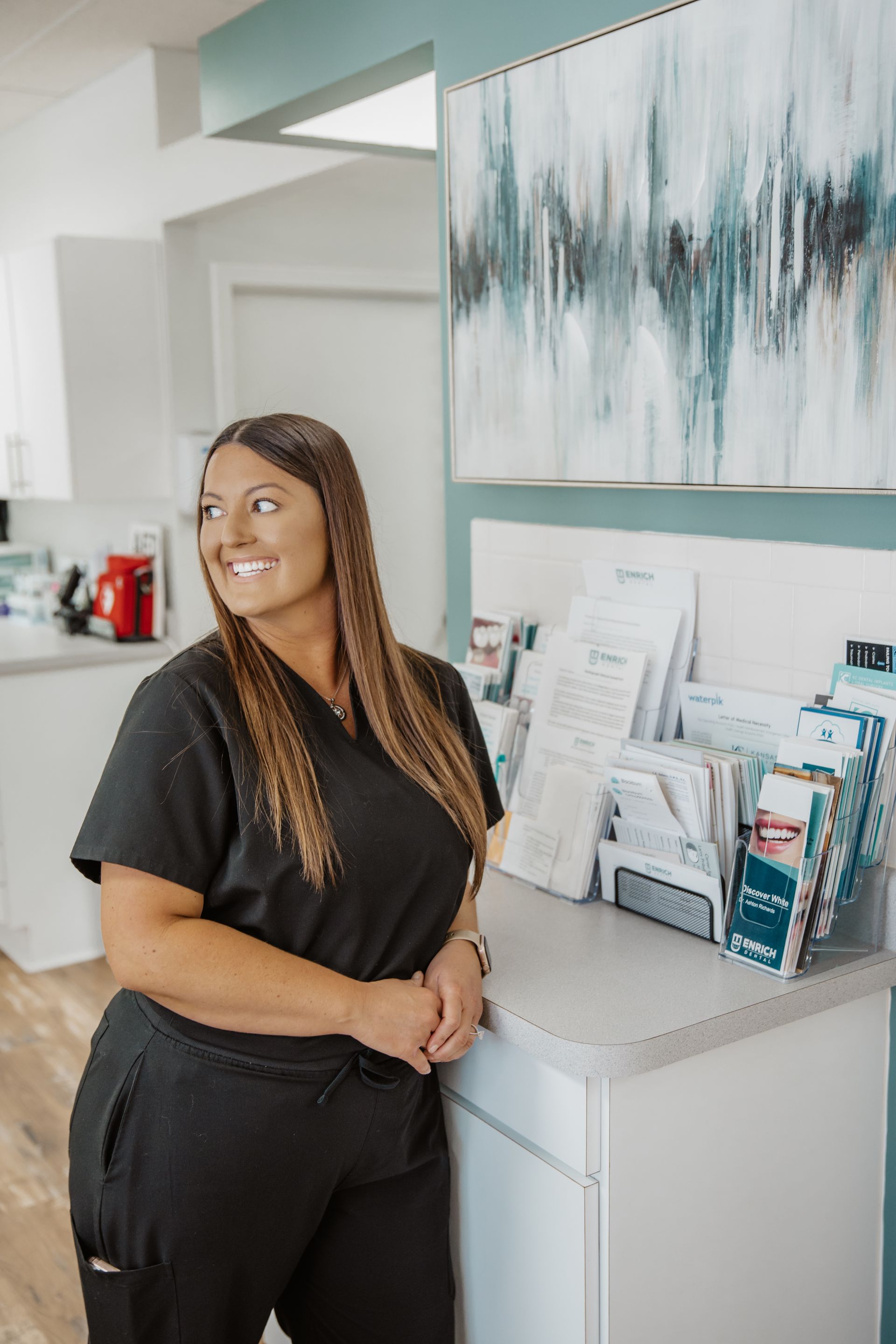 A woman in a black scrub is standing next to a counter in a dental office.