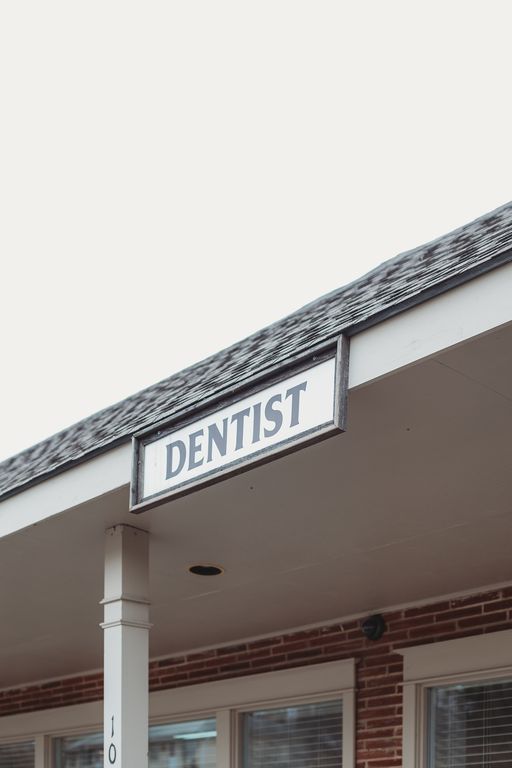 A dentist sign is hanging from the roof of a building.