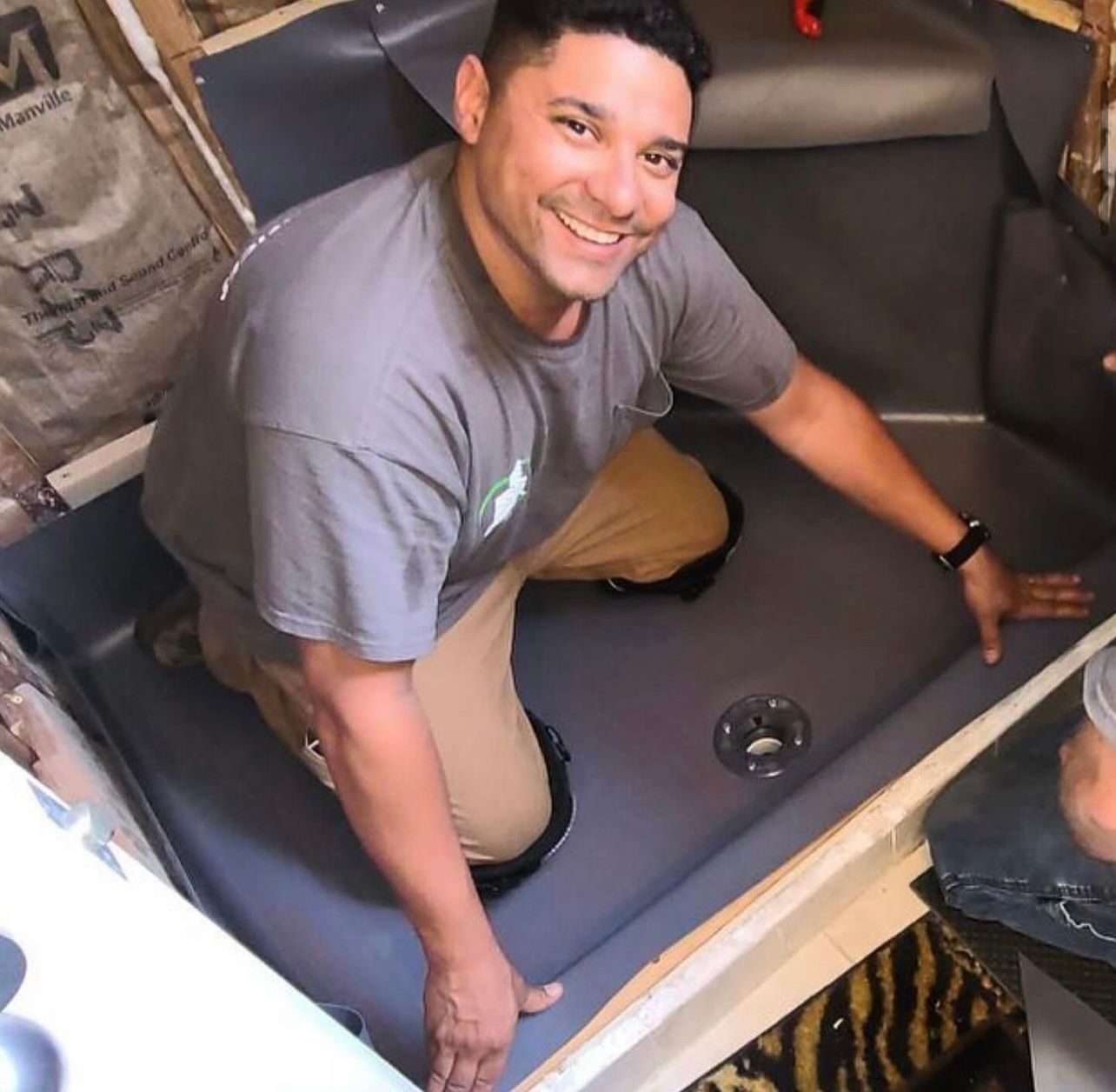 a man in a gray shirt is kneeling down in a bathroom