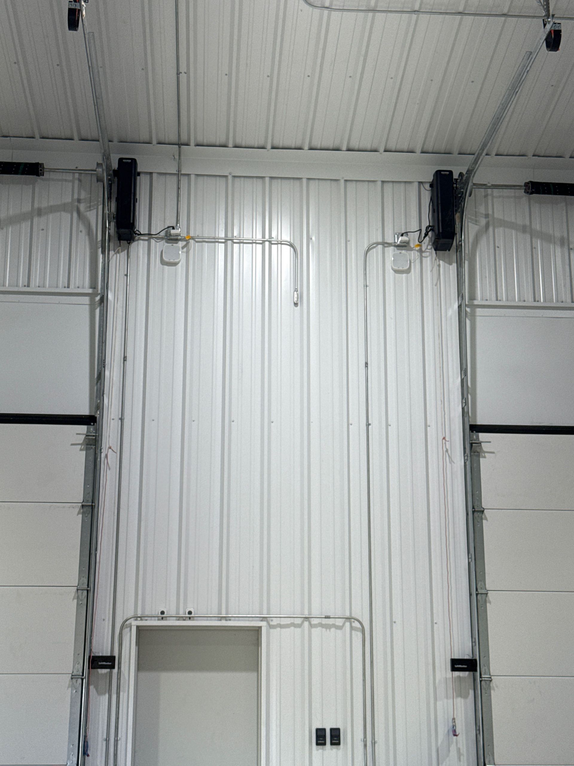 White industrial interior wall with hanging black speakers and a small door below the ceiling rafters