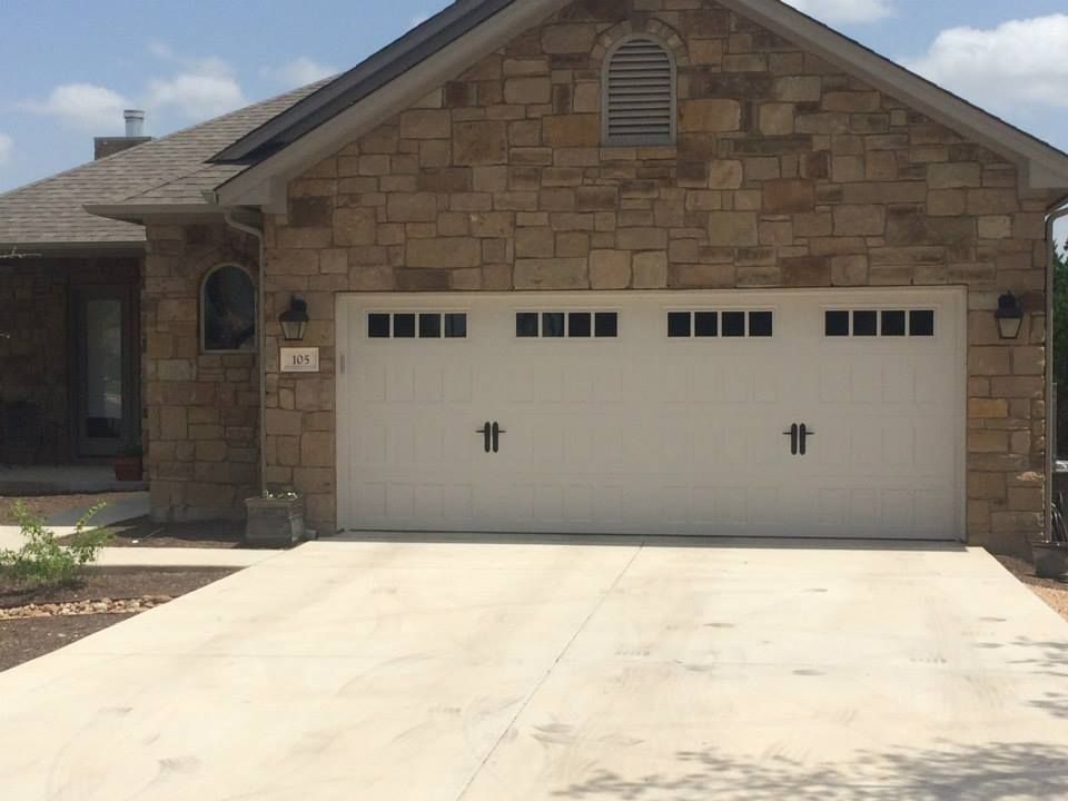 Single-story stone house with a white two-car garage and concrete driveway under a clear sky