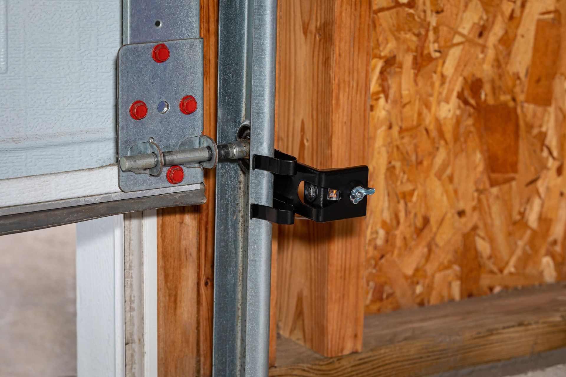 Close-up of a metal garage door hinge and latch mounted beside a wooden wall.