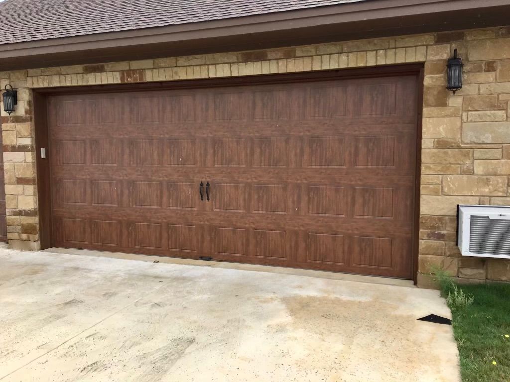 Brown double garage door on a stone house with a light concrete driveway