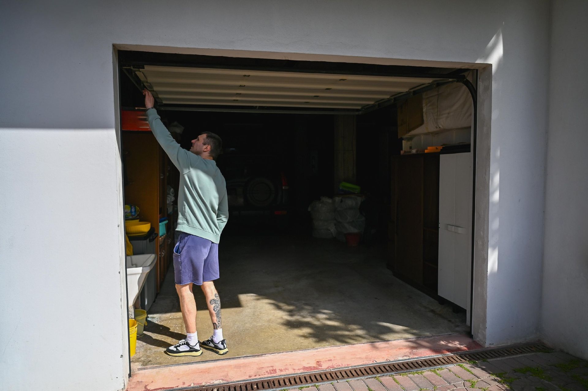 Person reaching up inside a partially open garage, with a white exterior and dim interior.