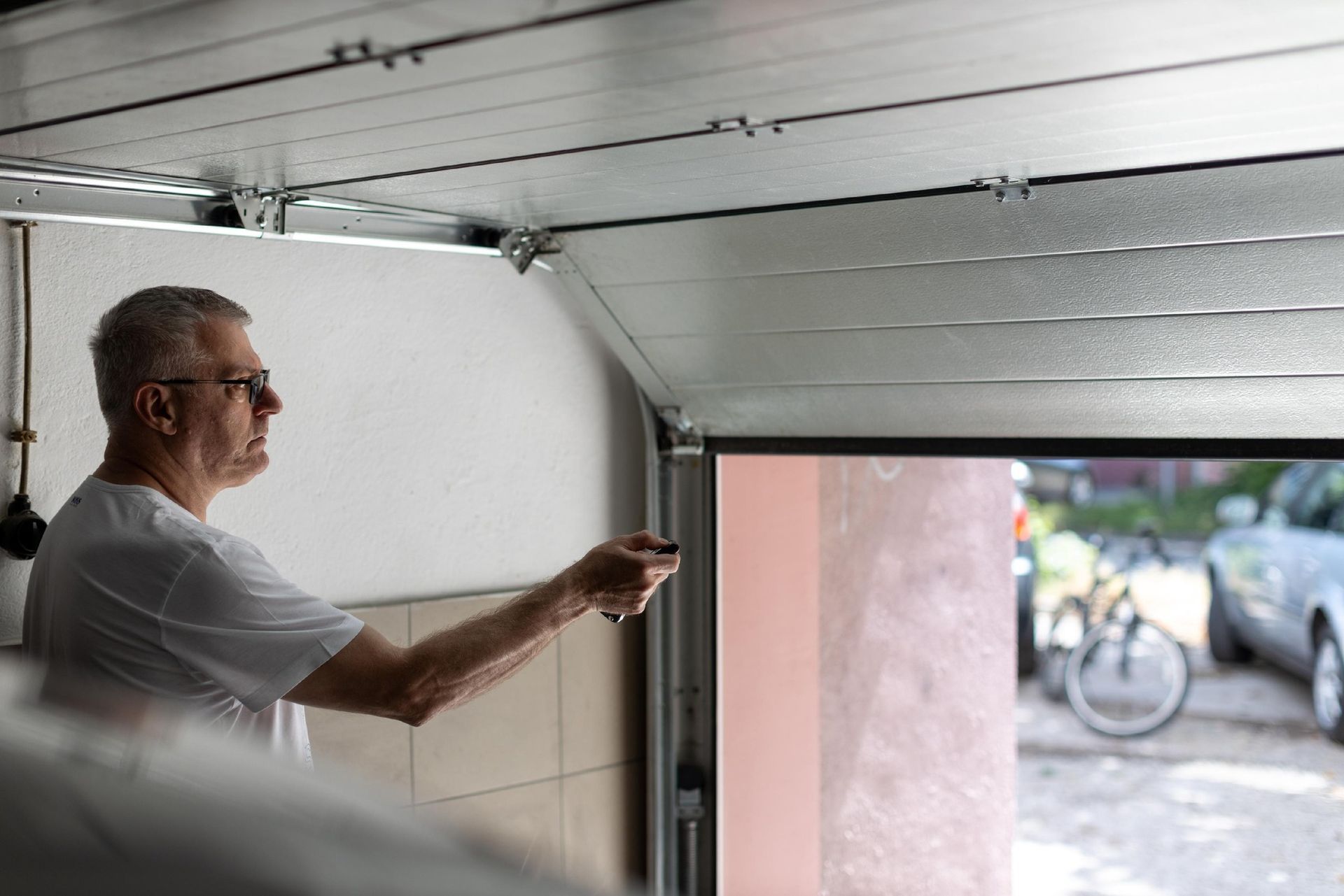 Man in white shirt standing in a garage doorway, looking and pointing outside at a bicycle.