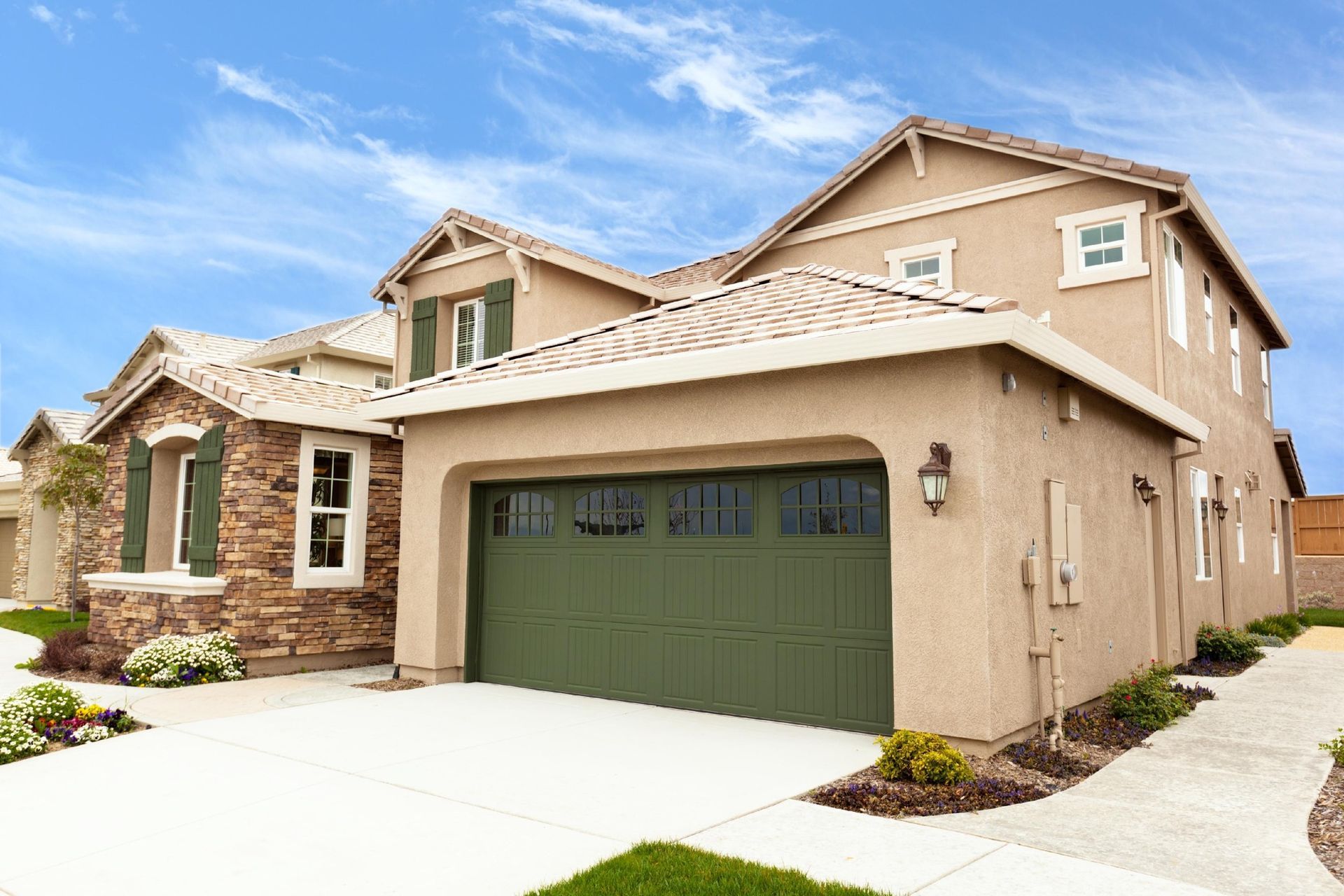 Suburban tan stucco house with green garage door and stone accents under a blue sky
