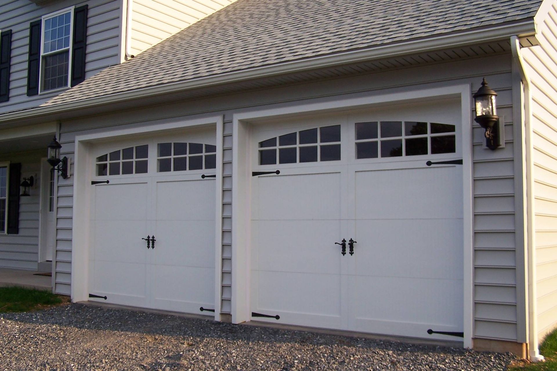 Two white garage doors with arched windows on a beige house exterior