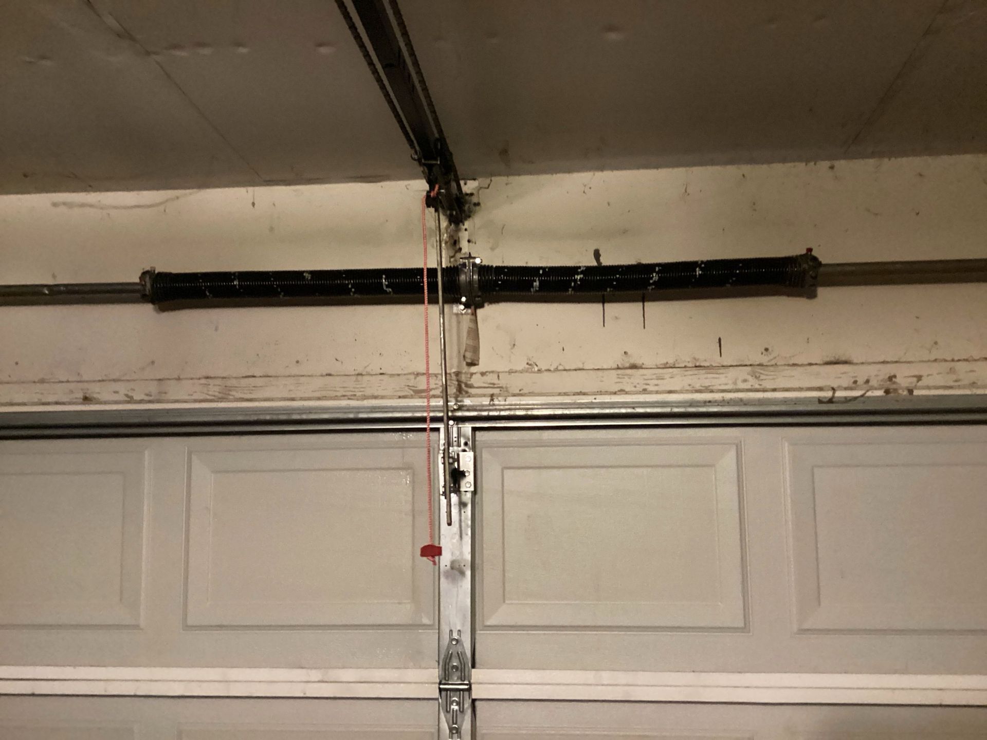 Garage door with a black torsion spring mounted above the panels and a hanging cable in the center.