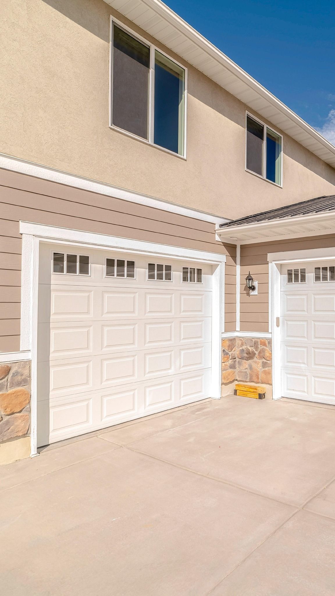 Two-story townhouse exterior with white garage doors and beige stucco walls under a clear blue sky