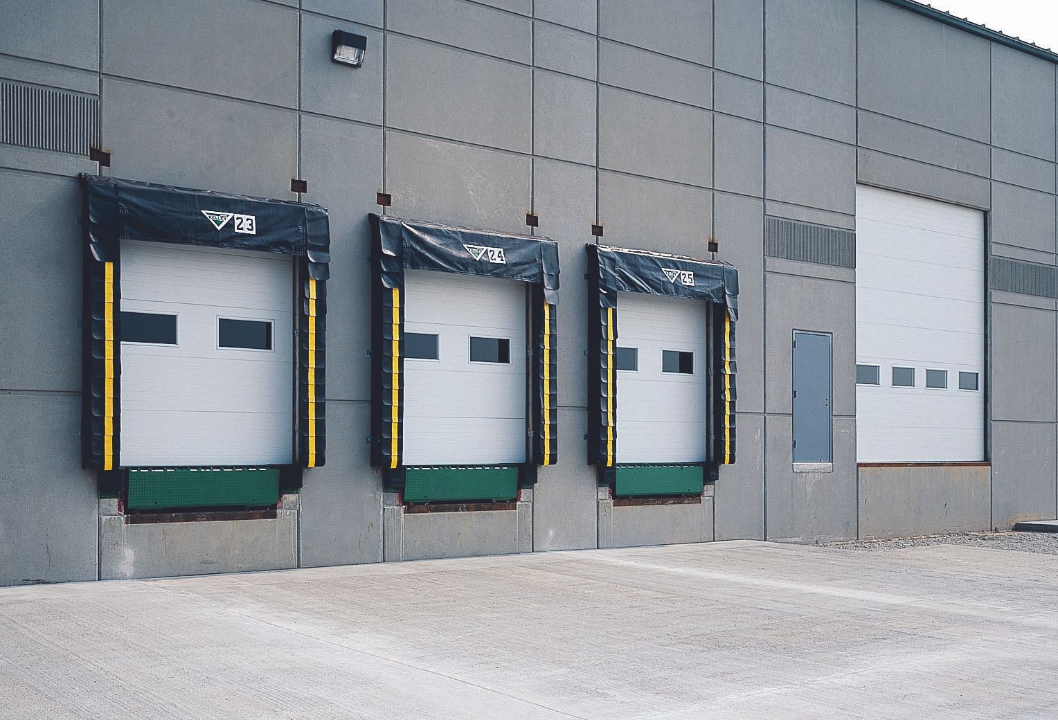 Three loading dock doors on a gray warehouse wall, with a large garage door to the right.