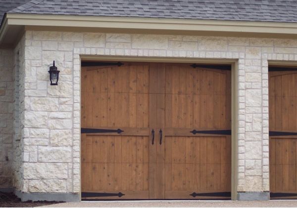 Wooden double garage door set in a stone facade with a small wall lantern on the left