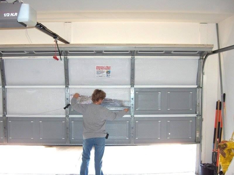 Person opening a gray garage door inside a garage with cleaning tools nearby