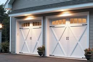 Two white carriage-style garage doors with X-bracing under warm exterior lights at dusk