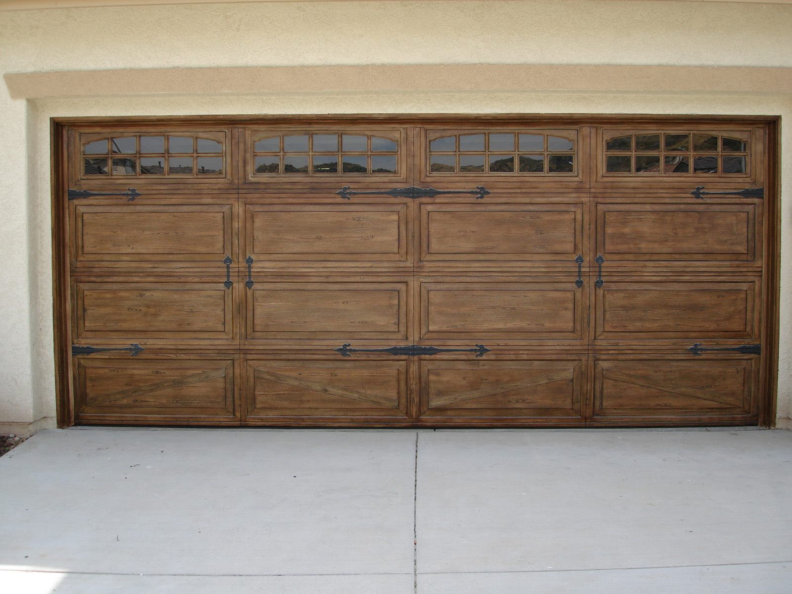 Wooden double garage door with small upper windows on a concrete driveway