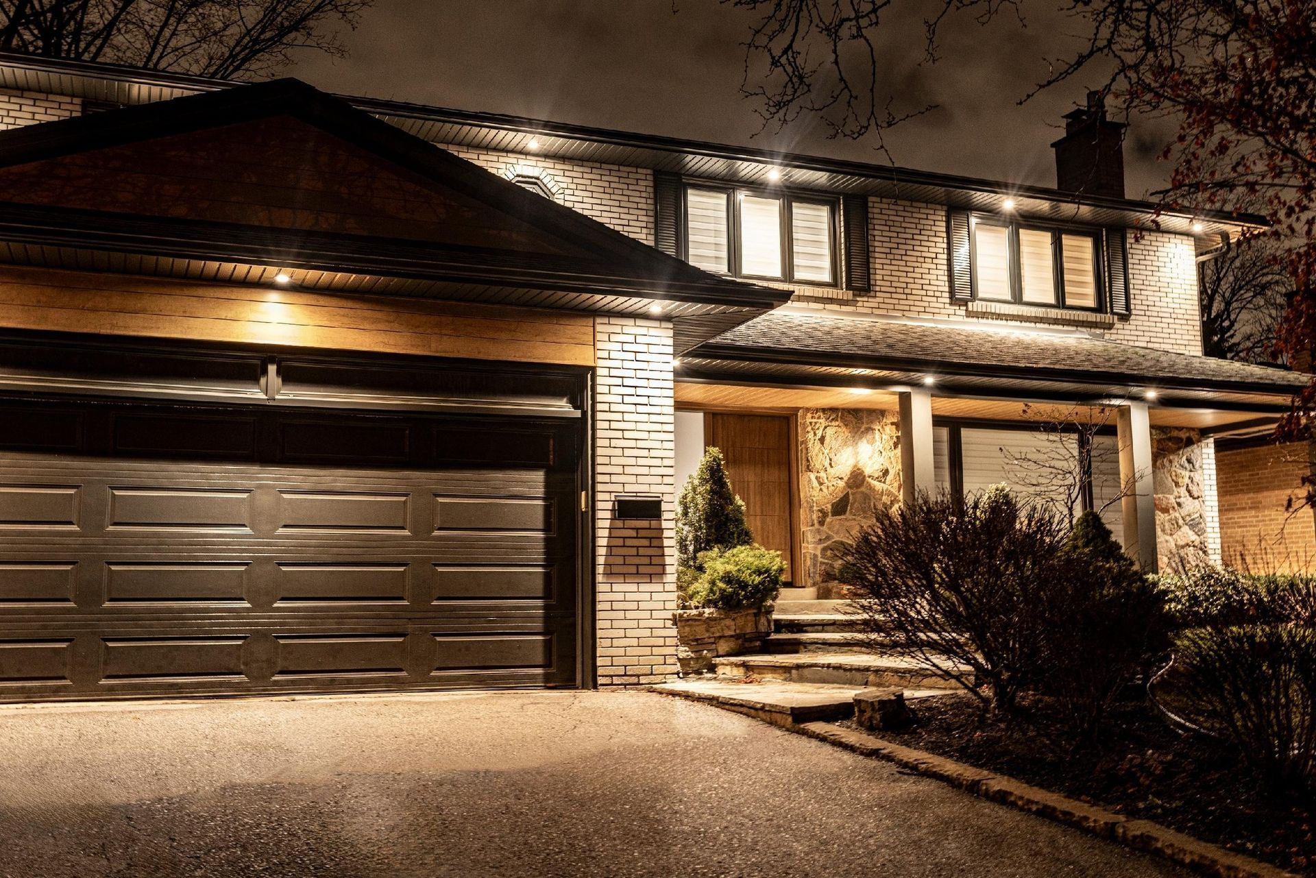 Illuminated two-story suburban house at night with a double garage and front porch light